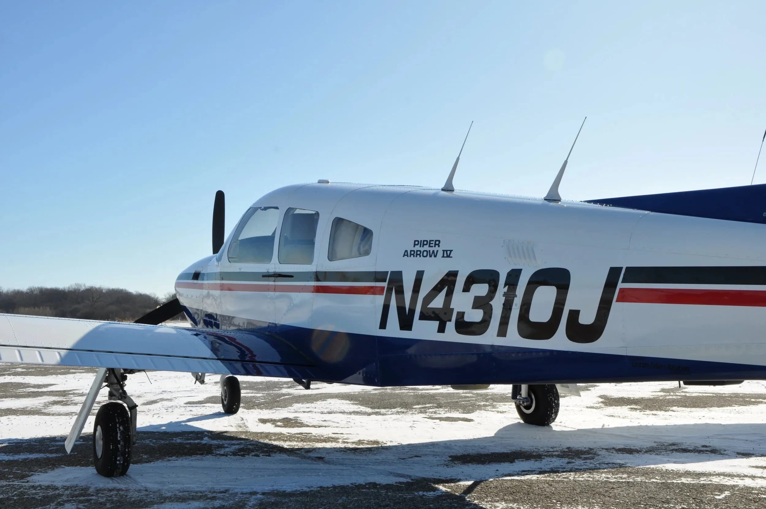 A side profile view of the white and blue Piper Arrow IV aircraft with registration N4310J on a snowy tarmac.