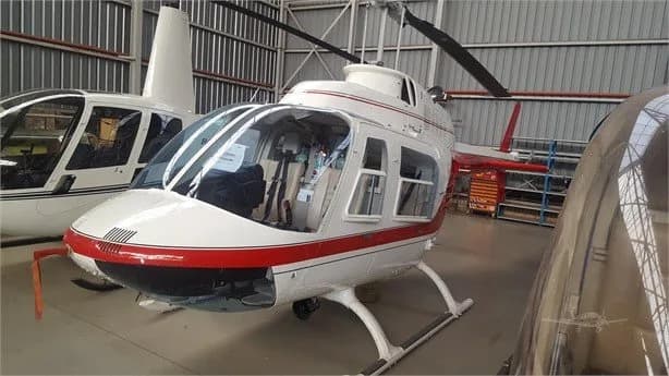 Bell Jet Ranger helicopter with red and white paint scheme inside a hangar.