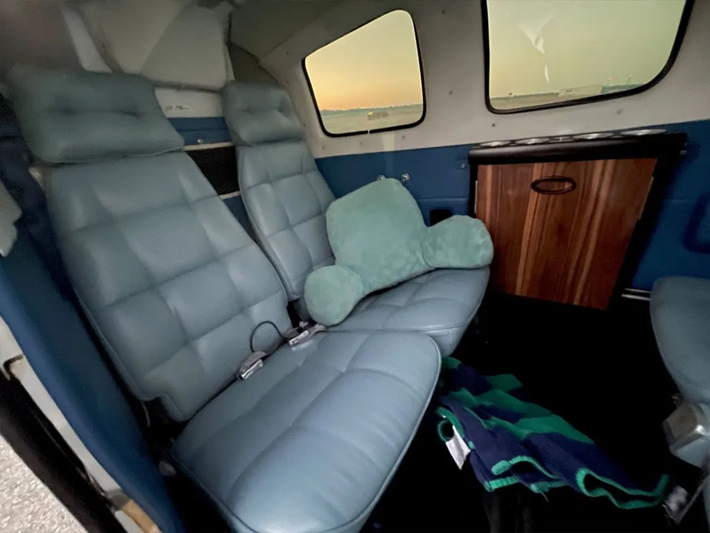 The aircraft's interior cabin shows light blue seats with a green pillow and a wooden cabinet on the side.