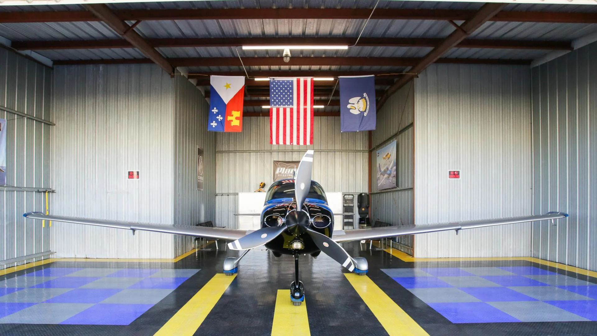 A front view of a blue and silver Cirrus SR22 aircraft with registration N444JH inside a hangar.