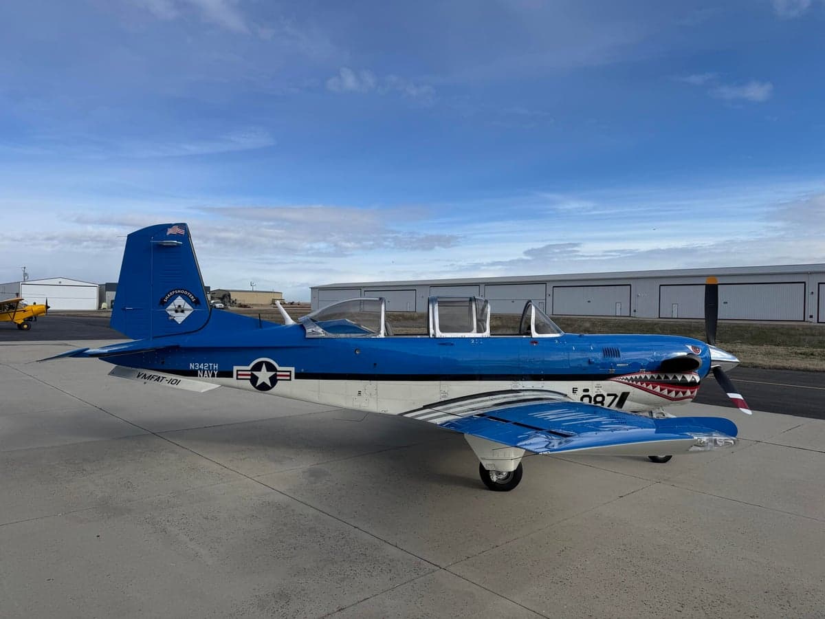 A blue and white SIAI-Marchetti SF.260 is parked on the tarmac with a shark mouth paint scheme.