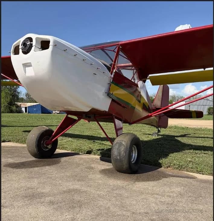 A close-up, low-angle view of the front of a red and yellow ultralight aircraft with a white nose cowl and large tires.