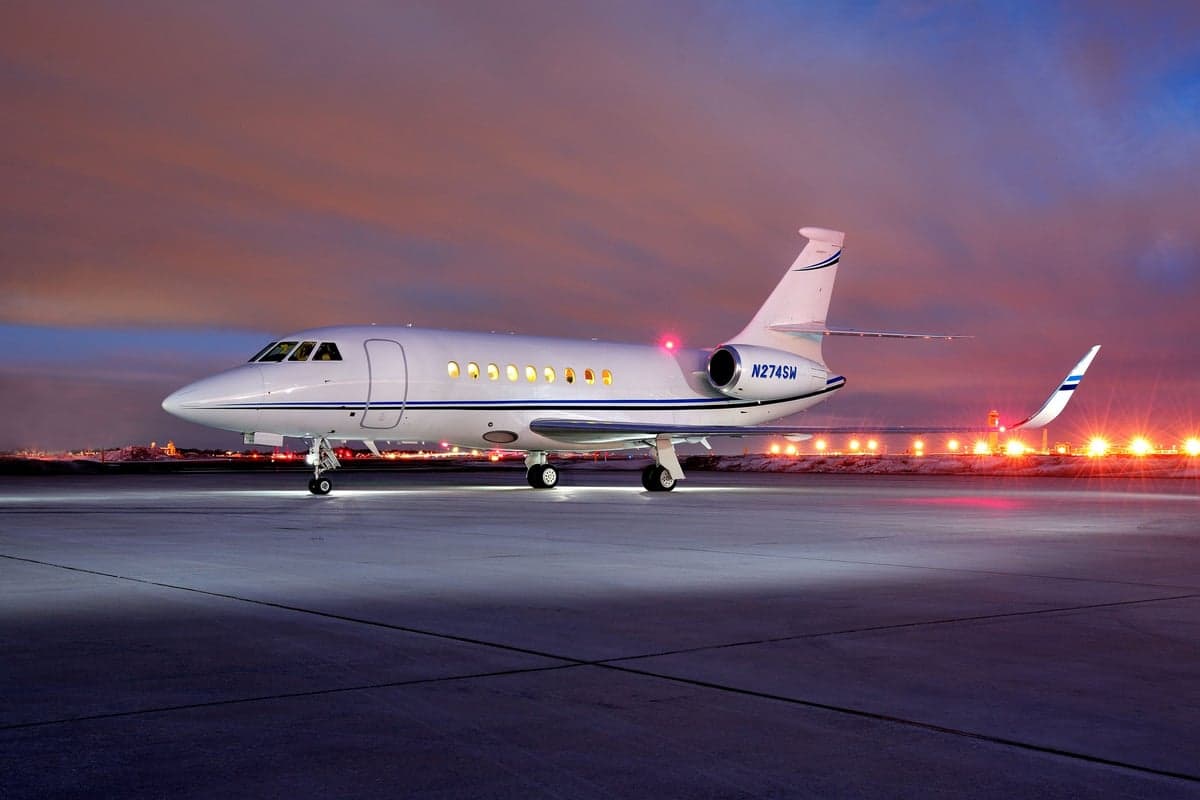 A Falcon aircraft sits on the tarmac at dusk.