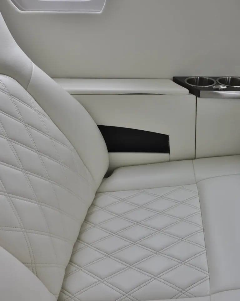 Close-up of a white leather aircraft seat with diamond stitching and a cup holder console.