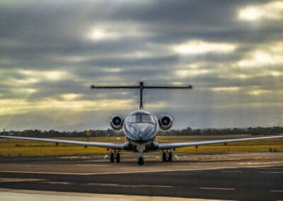Front view of a black Pilatus PC-24 jet on the tarmac with a cloudy sky.