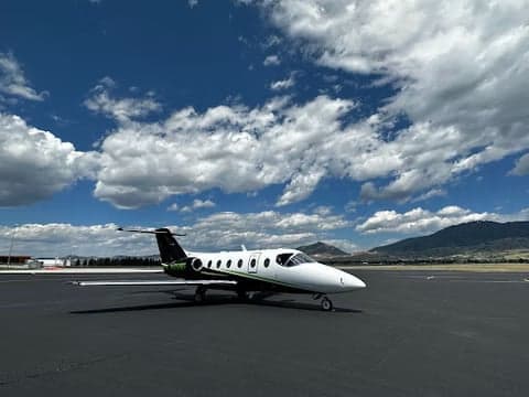 A white and black jet parked on the tarmac with mountains in the background.