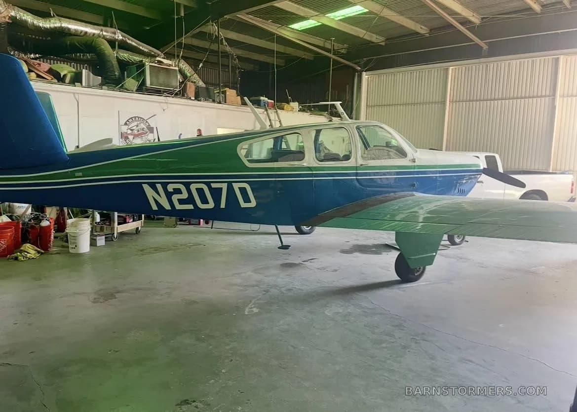 A blue and green single-engine propeller aircraft (N207D) parked inside a hangar, showing its side profile and wing.