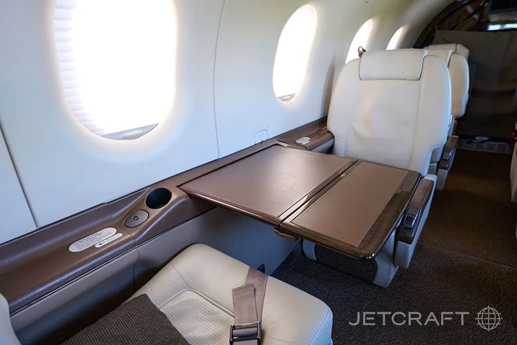 A close-up of a light cream leather seat and a brown fold-out table next to a window in the aircraft cabin.