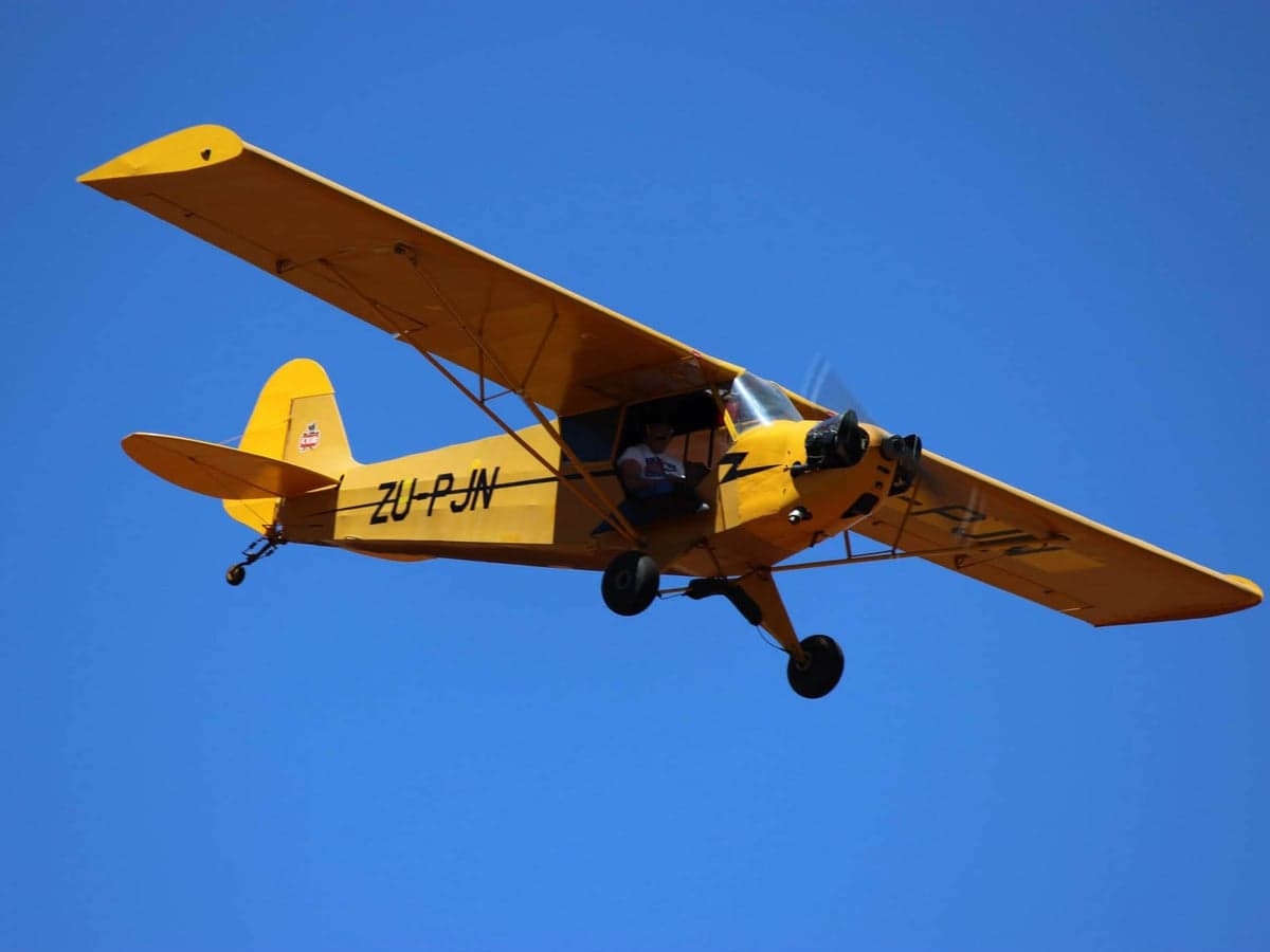 A yellow Piper Cub in flight against a clear blue sky.