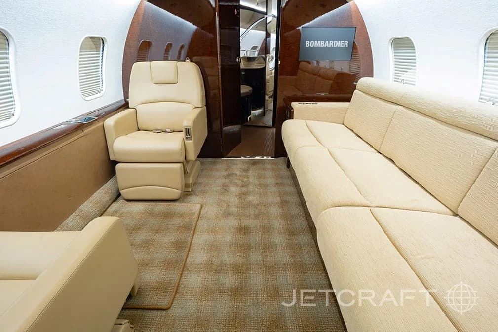 A section of the aircraft cabin with a long beige sofa and a single beige leather seat.