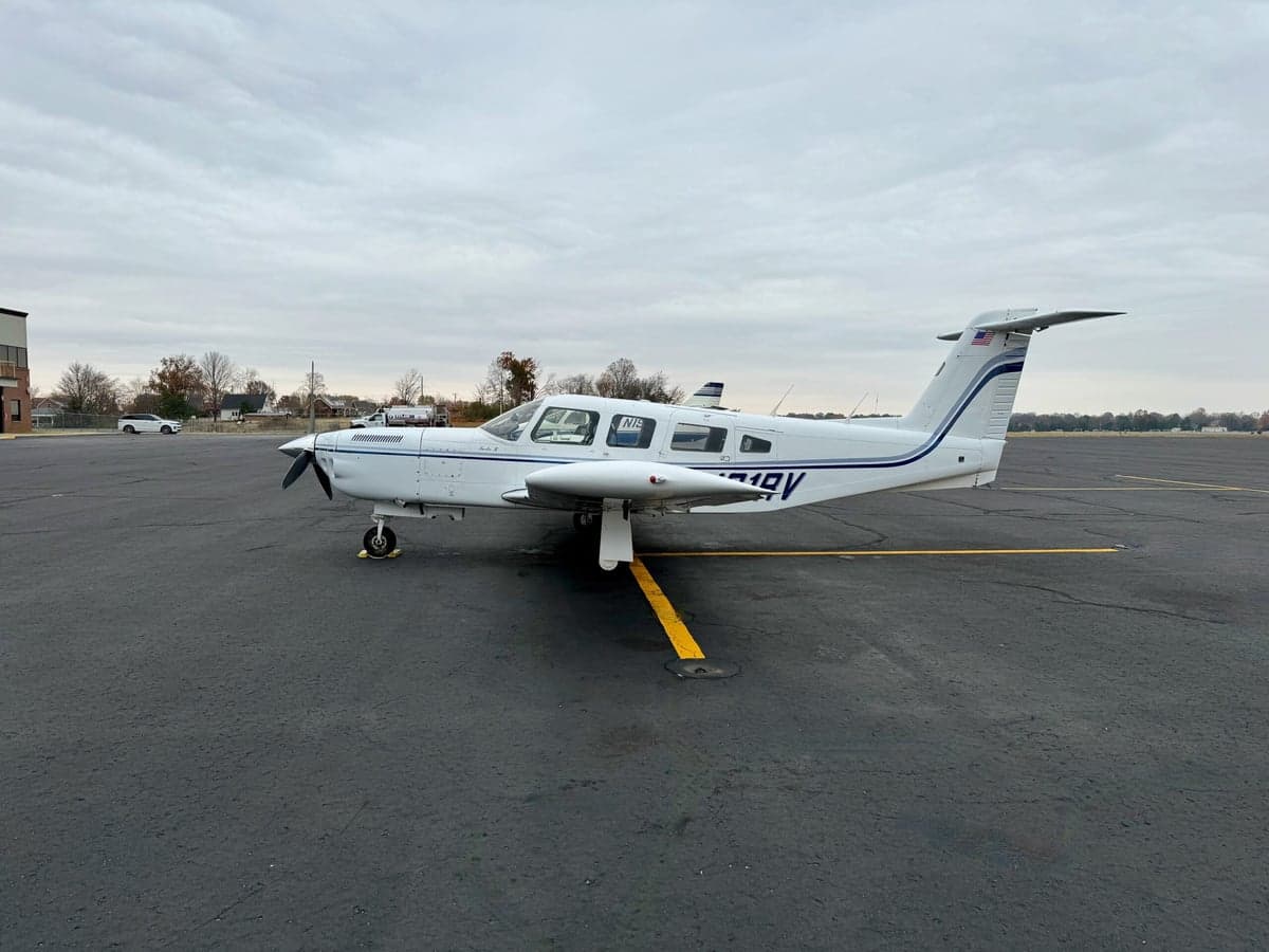 Side view of a white single-engine propeller aircraft with blue stripes and registration N191RV on an airfield.
