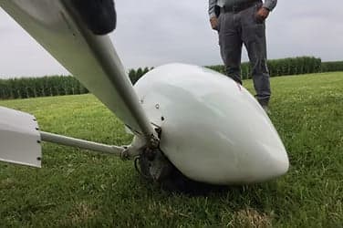 Close-up of the nose and propeller of an aircraft on a grassy field.