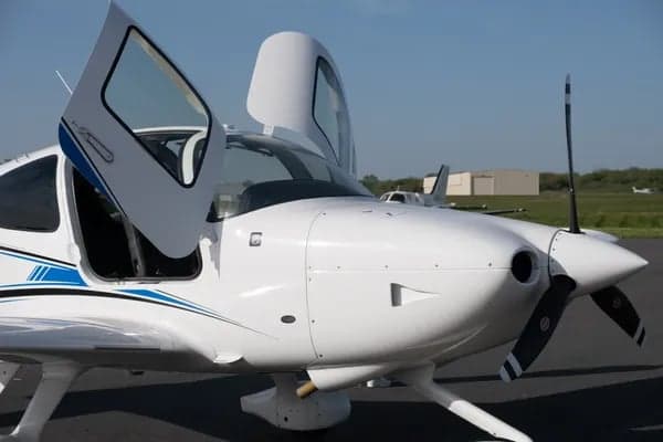 Close up of a white Cirrus aircraft with doors open on the tarmac.