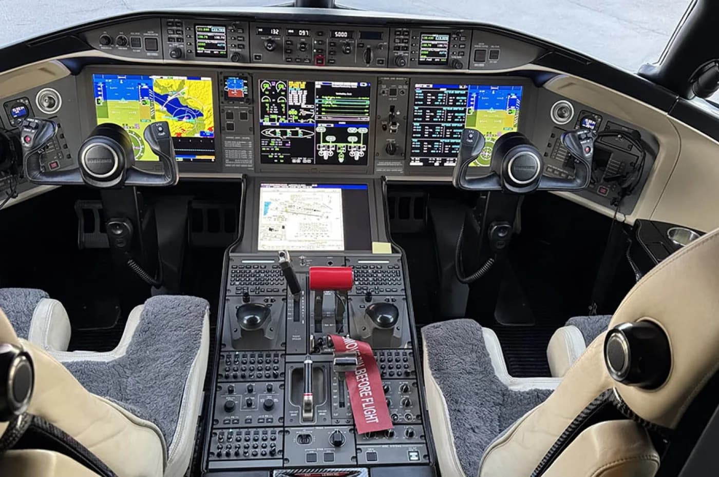 The modern glass cockpit of a business jet, featuring multiple large displays, yokes, and a central throttle quadrant with a 'REMOVE BEFORE FLIGHT' tag.