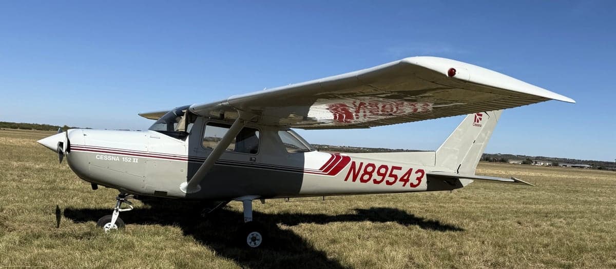 A Cessna 152 II aircraft with registration number N89543 parked on a grassy field, showing the side profile.