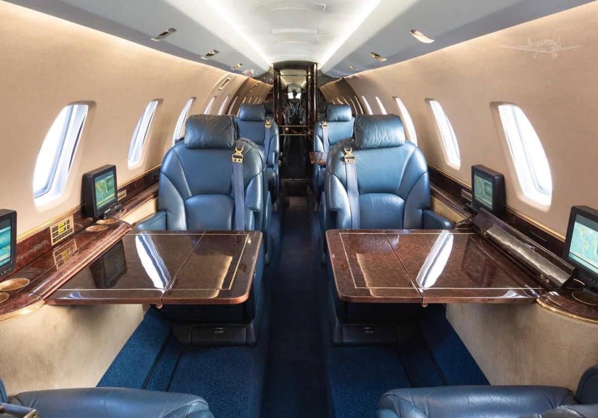 A view of the interior cabin of a private jet with blue leather seats and wood tables.