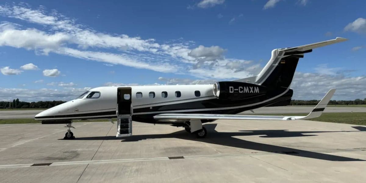 Side view of a black and white Phenom 300 aircraft with the airstair door open on the tarmac.