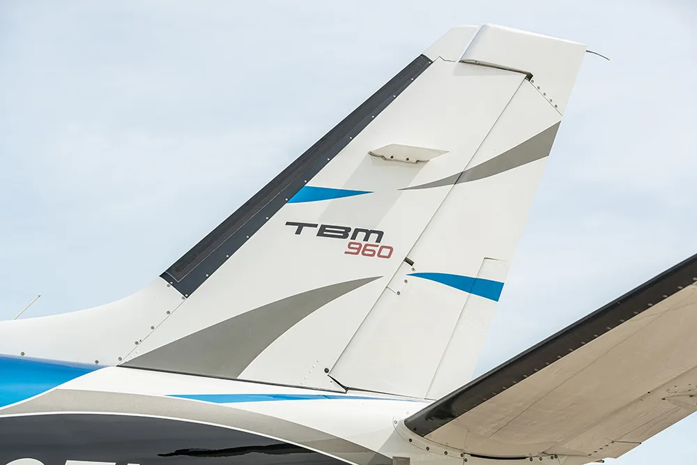 A close-up view of the white, blue, and black tail of a TBM 960 aircraft.