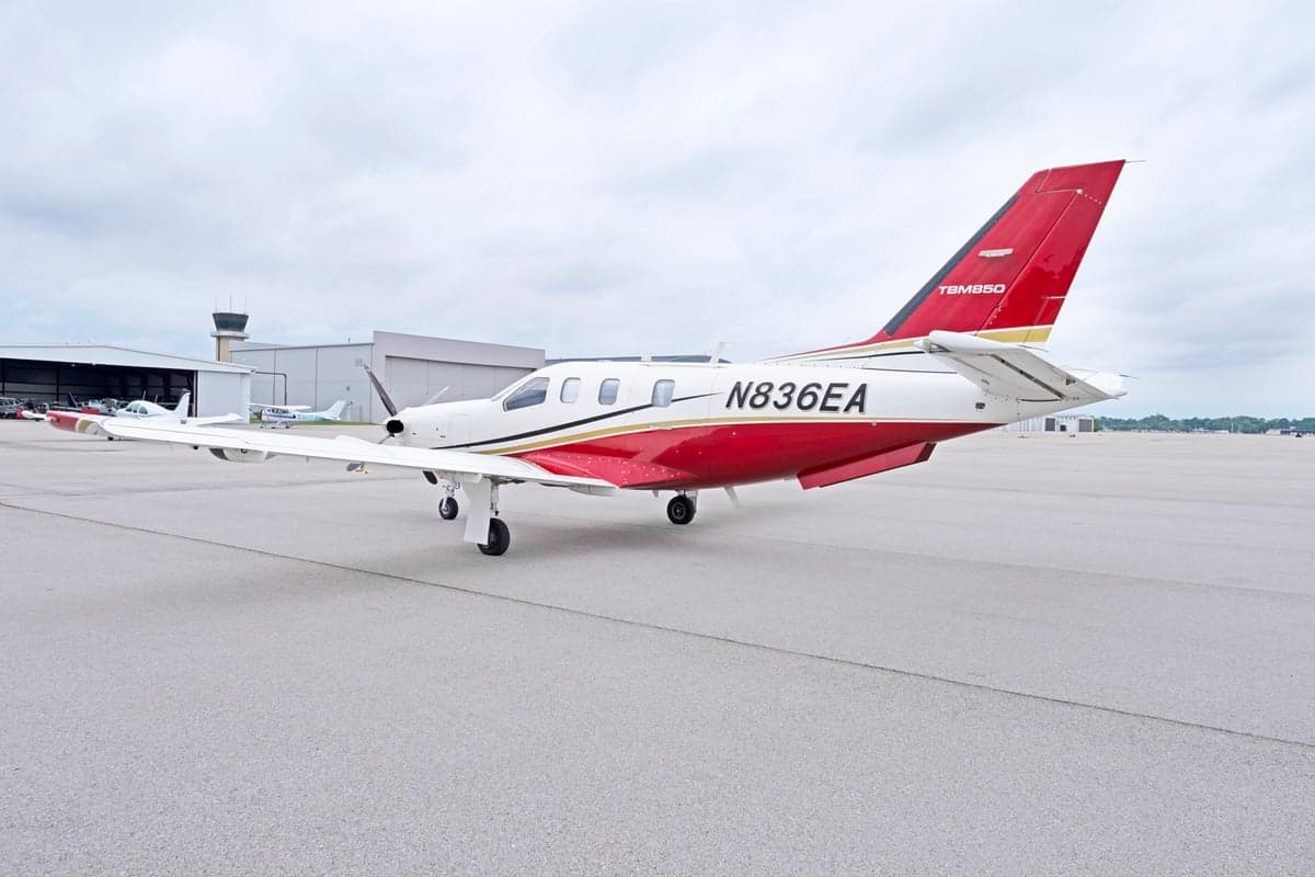 Side view of the TBM 850 aircraft N836EA on the tarmac with a control tower in the background.