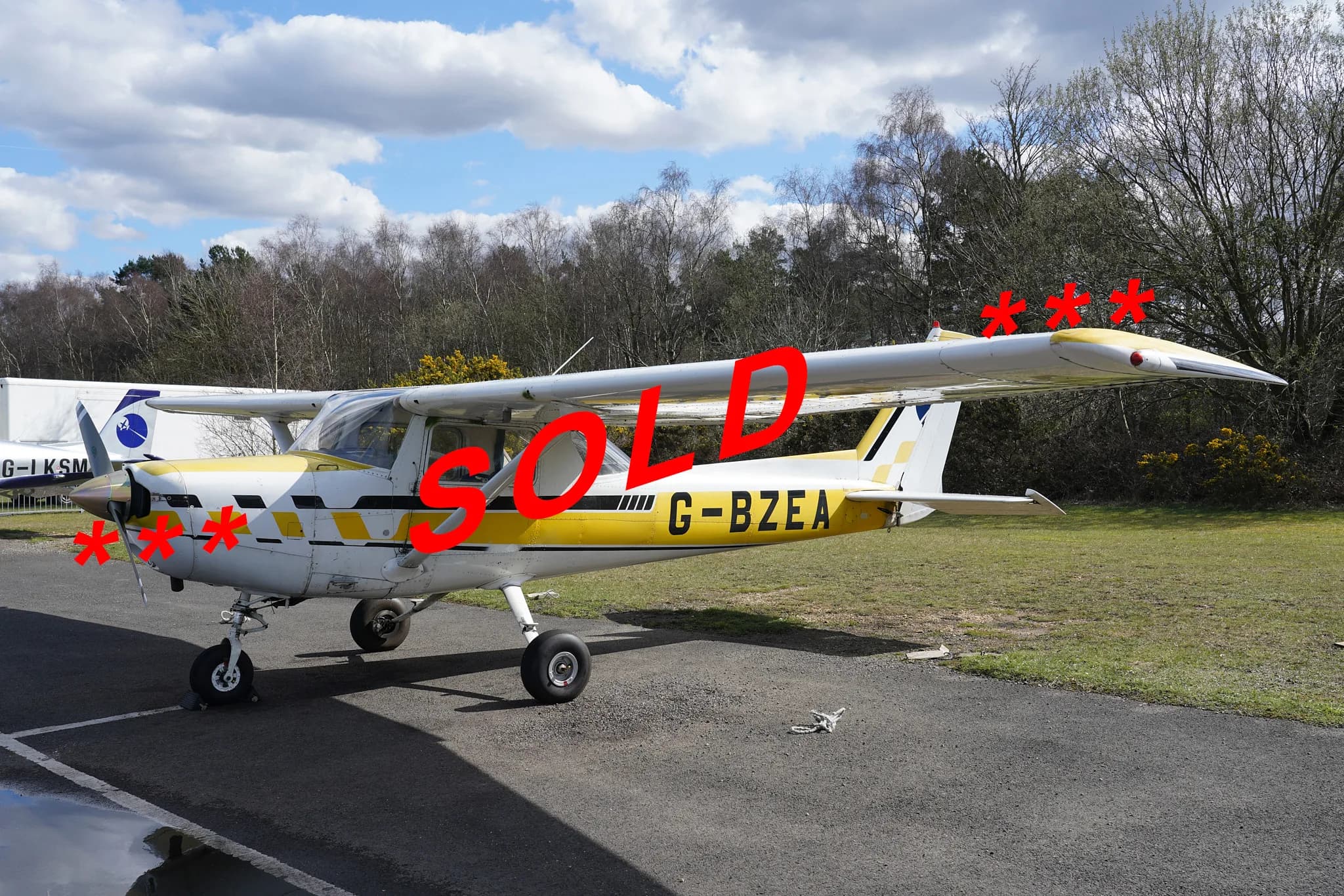 A yellow and white Cessna 150 with registration G-BZEA and "SOLD" overlaid, parked on an airfield tarmac.