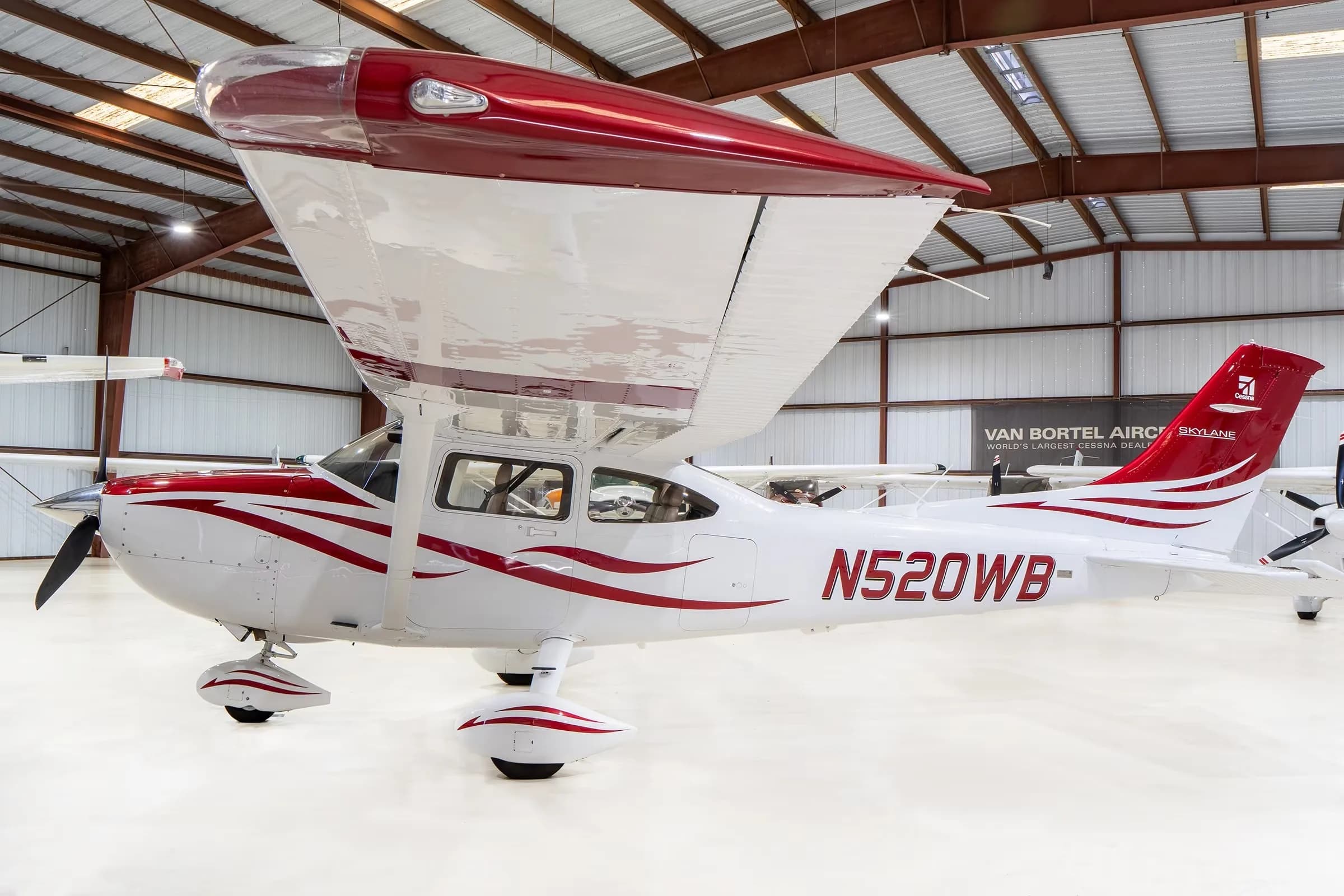 A white Cessna Skylane N520WB with red and grey stripes, parked in a hangar, viewed from the front-right.