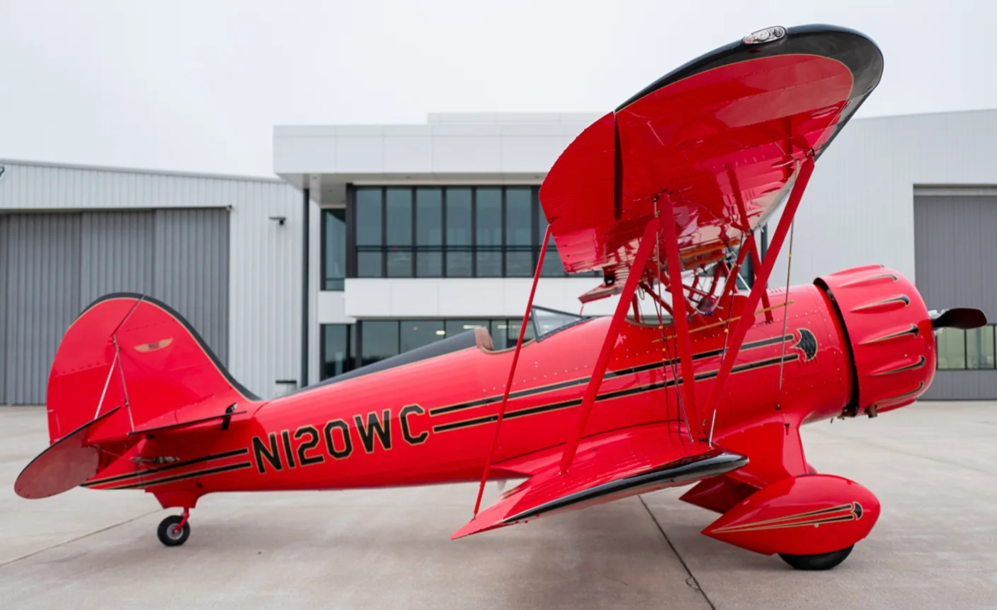 A red biplane with black accents and the tail number N120WC is parked on the tarmac.