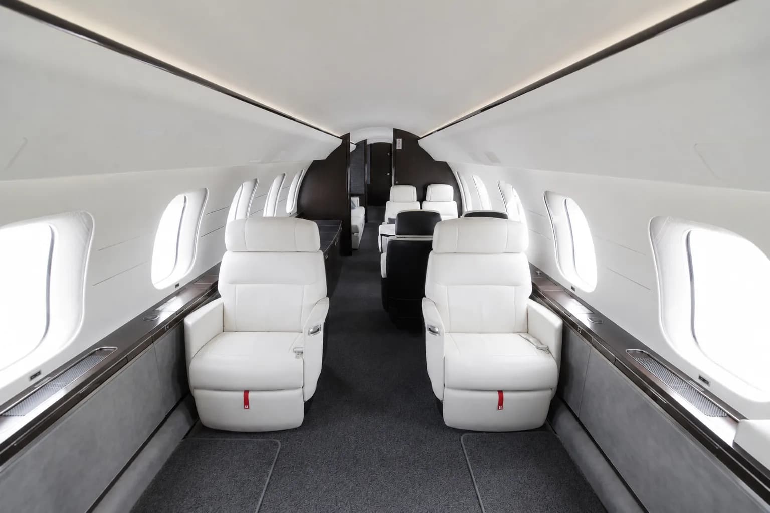 The spacious main cabin of a private jet, featuring rows of white leather seats and large windows.