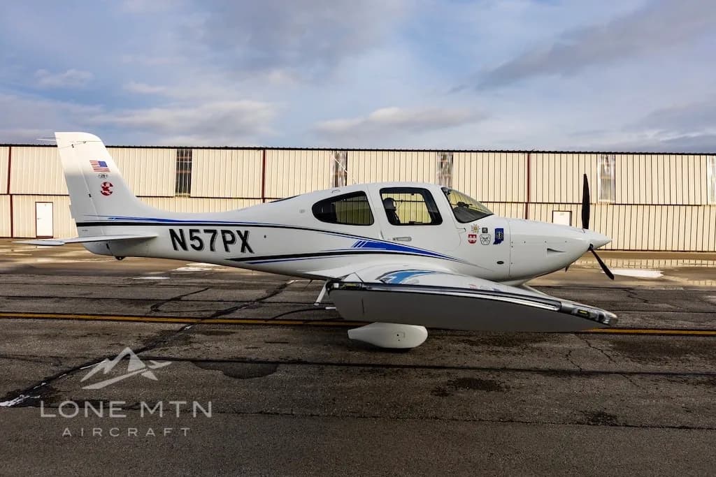 A side view of a white Cirrus SR22 aircraft with blue and black stripes, tail number N57PX, parked on an airport tarmac.