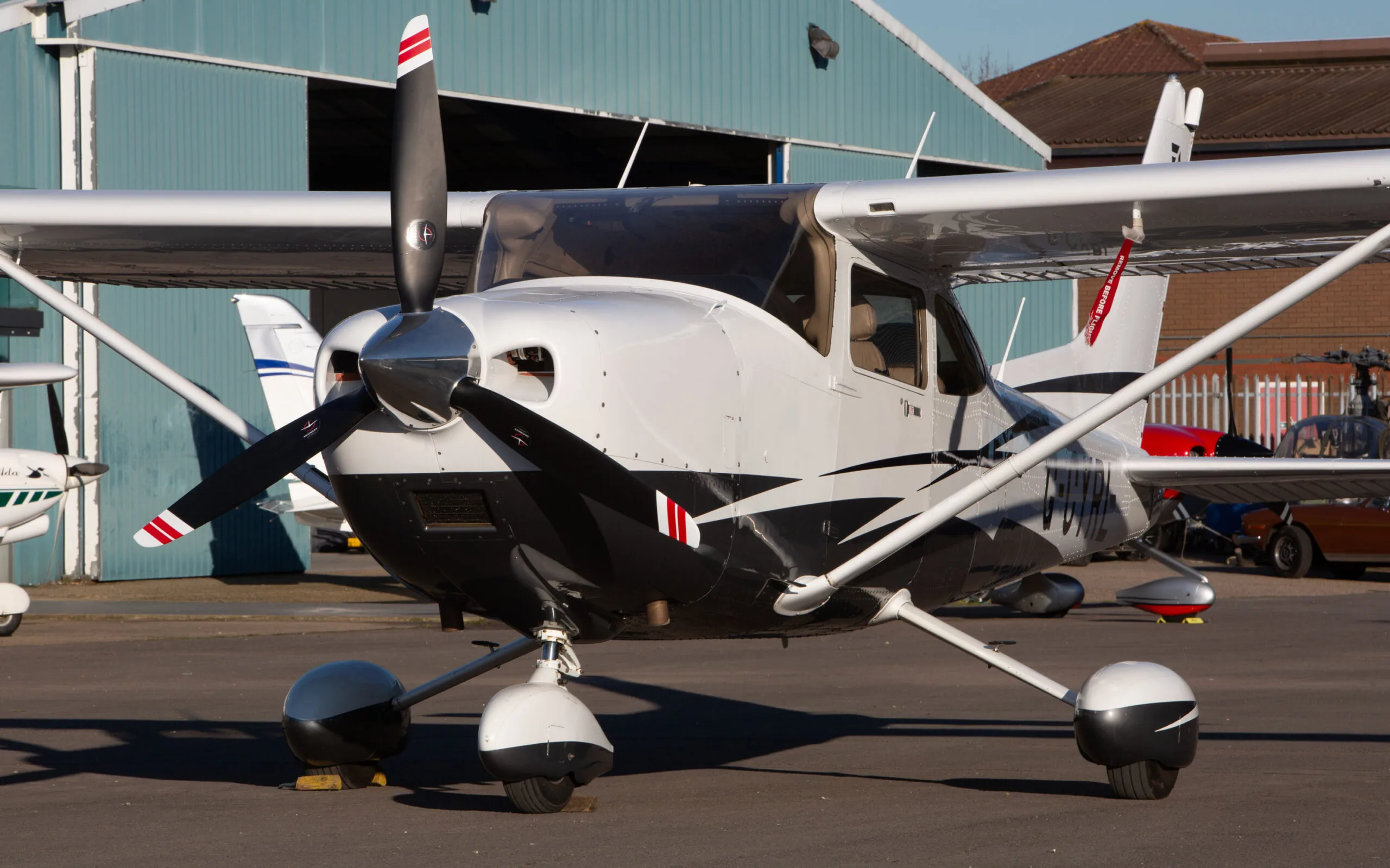 A white and black Cessna 182T (G-CYRL) parked on an airfield with a hangar in the background.