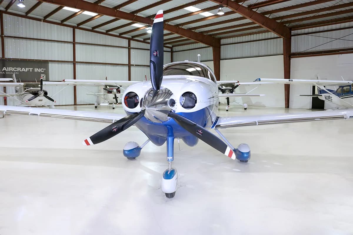 A white and blue Cessna TTx aircraft is parked in a hangar, viewed directly from the front.