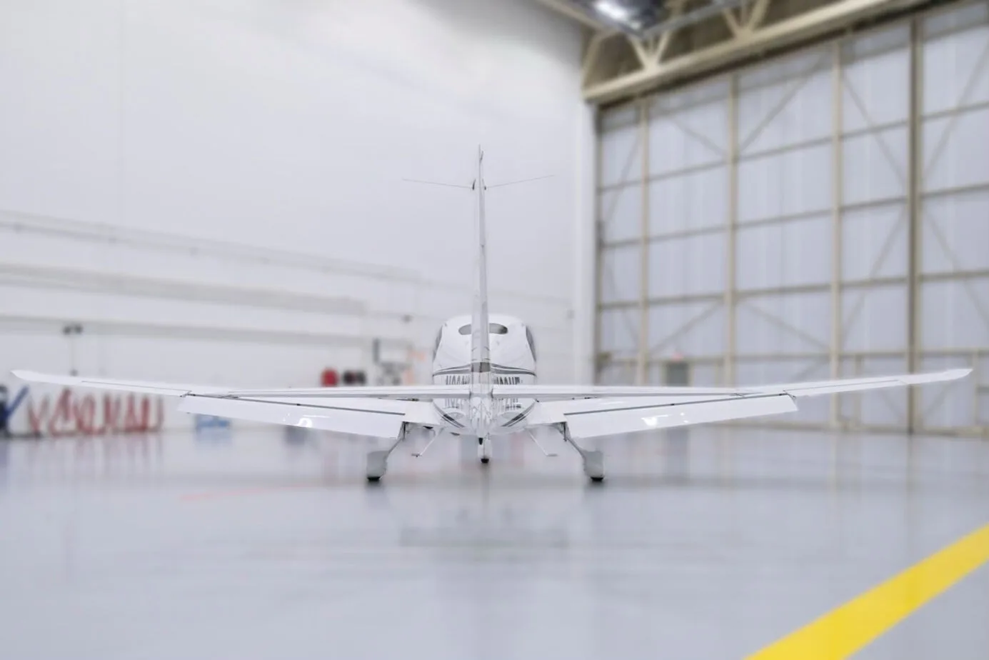 A rear view of a white Cirrus SR22 aircraft, N322NE, parked in a hangar.