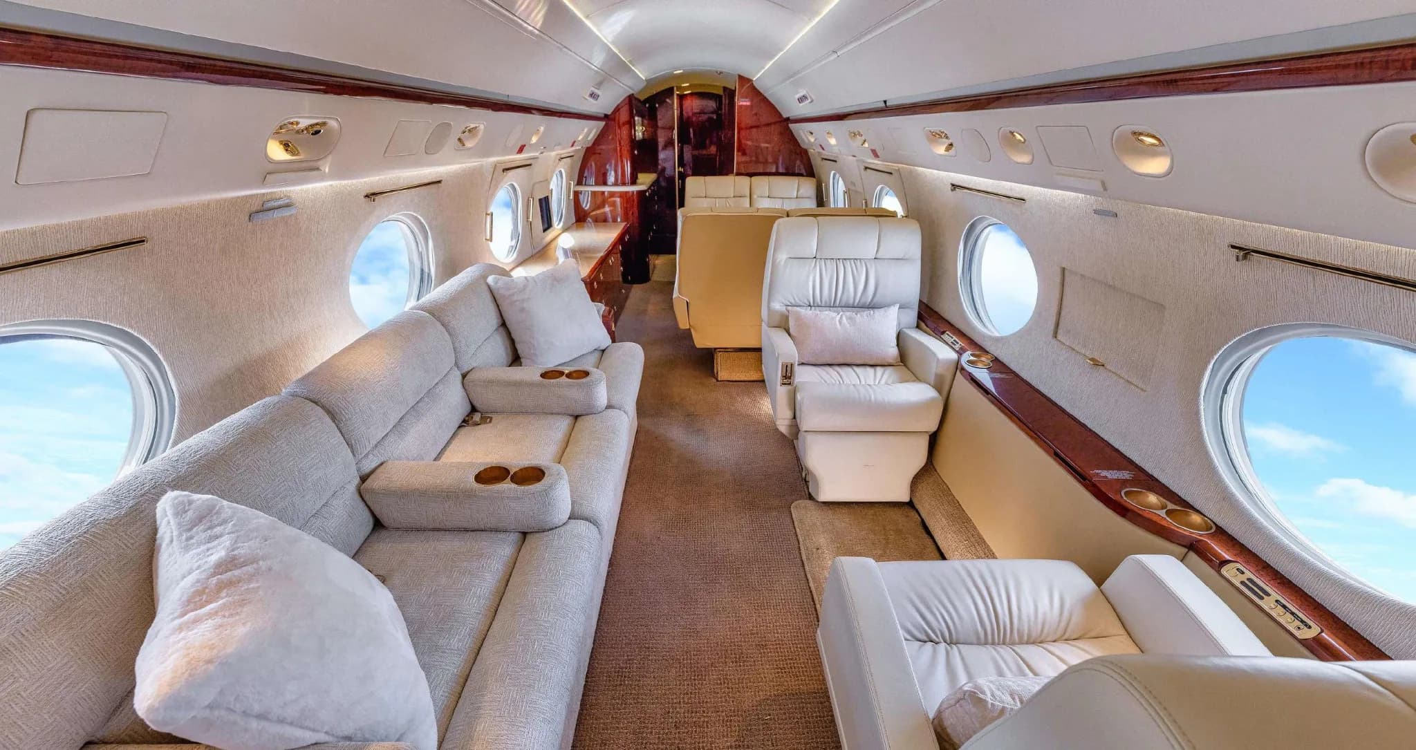 A wide view of the Gulfstream G550 cabin interior, featuring a comfortable cream sofa and individual seats.