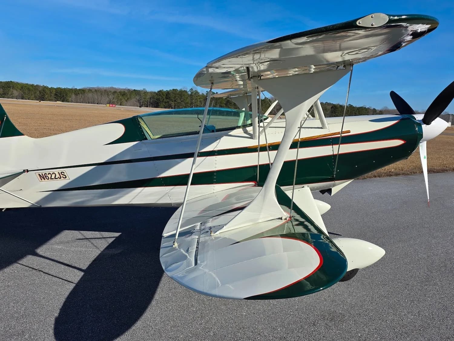 A close-up side view of the green and white biplane N622JS on an airfield.
