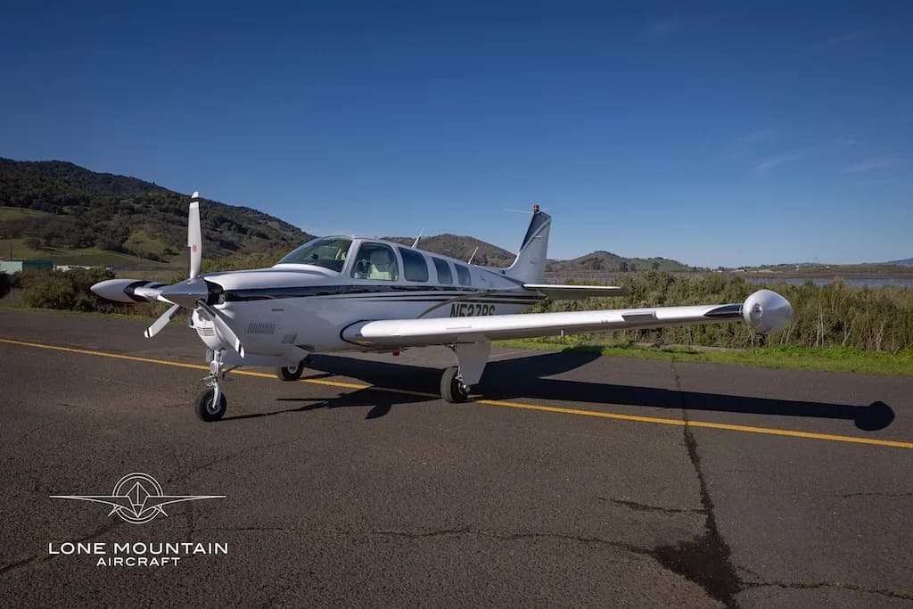 A front three-quarter view of a white Beechcraft Baron N527RS with black and gold stripes parked on an asphalt runway.