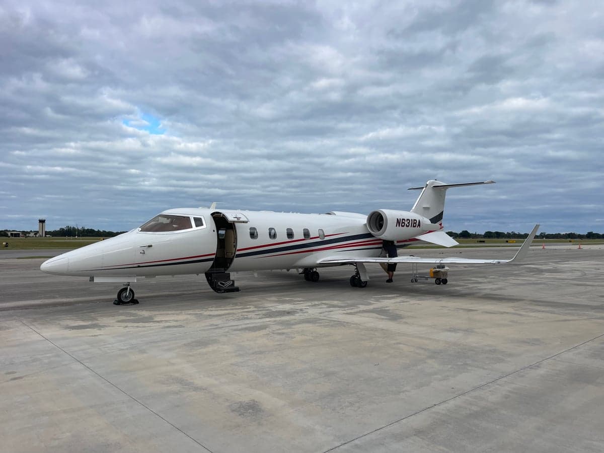 A white Learjet with red and black stripes and registration N631BA is parked on a tarmac with its door open.