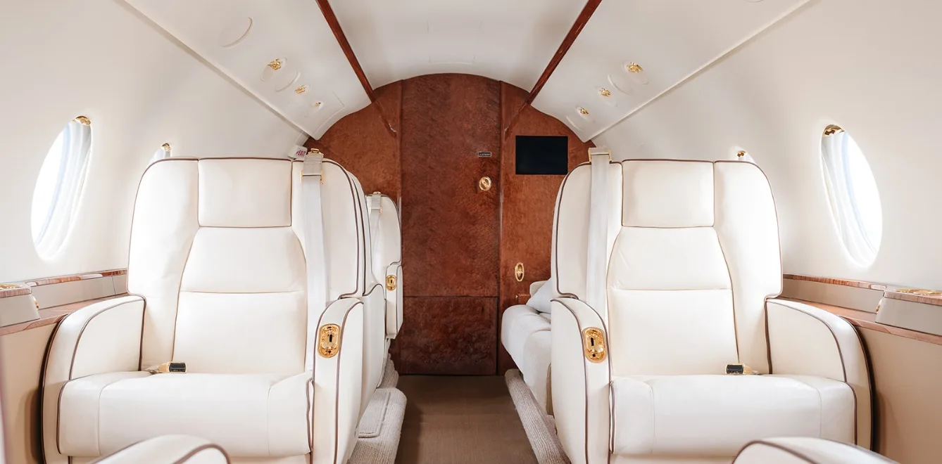 View of the aircraft interior with white leather seats and wood accents.