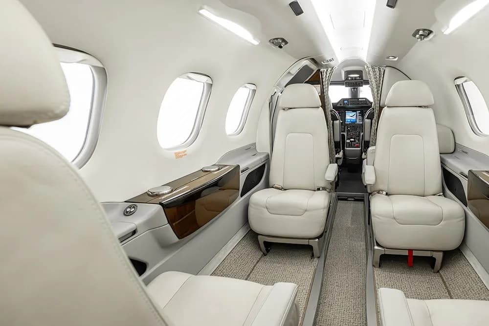 The interior of the Embraer Phenom 100E cabin, featuring cream leather seats and a view towards the cockpit.