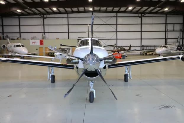 Front view of a Pilatus PC-12 in a hangar with other aircraft.