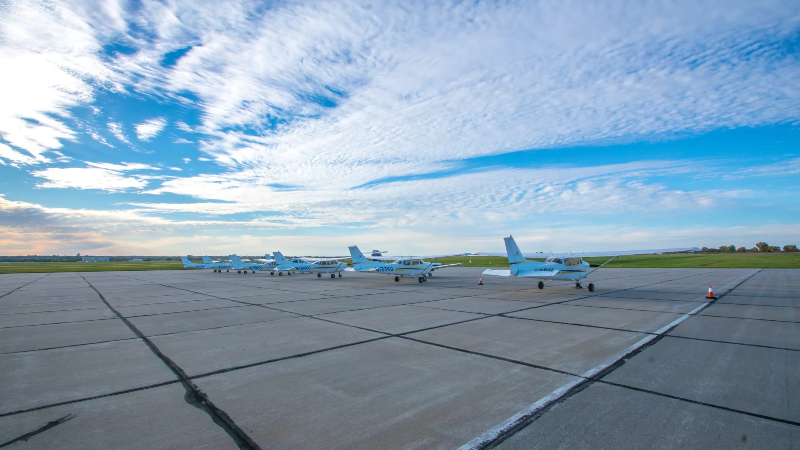 Line of Cessna 172 aircraft on the ramp under a blue sky.