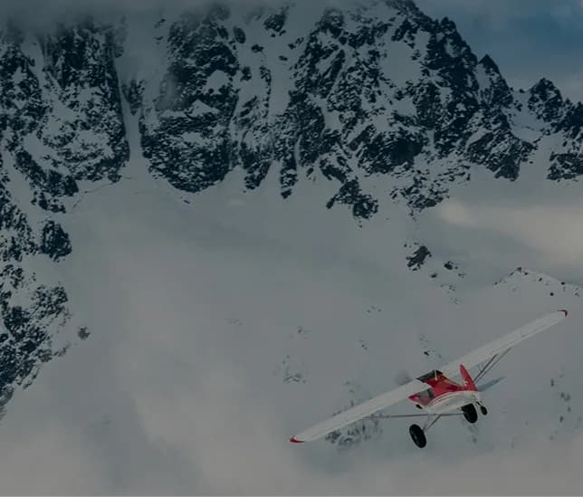 Red and white aircraft flying near a snowy mountain.