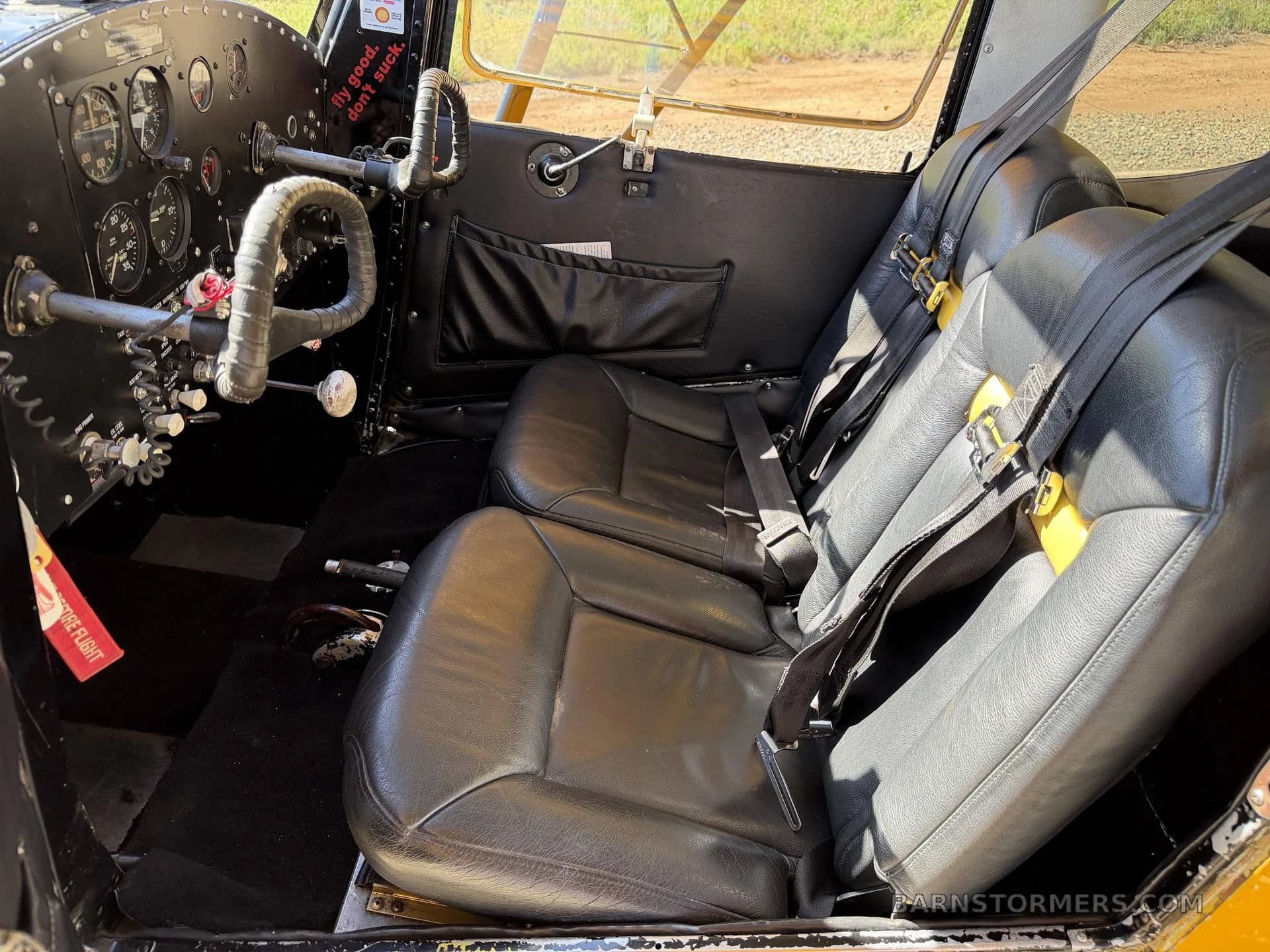 The aircraft's interior shows two black leather seats with yellow accents and seatbelts, viewed from the cockpit towards the passenger area.