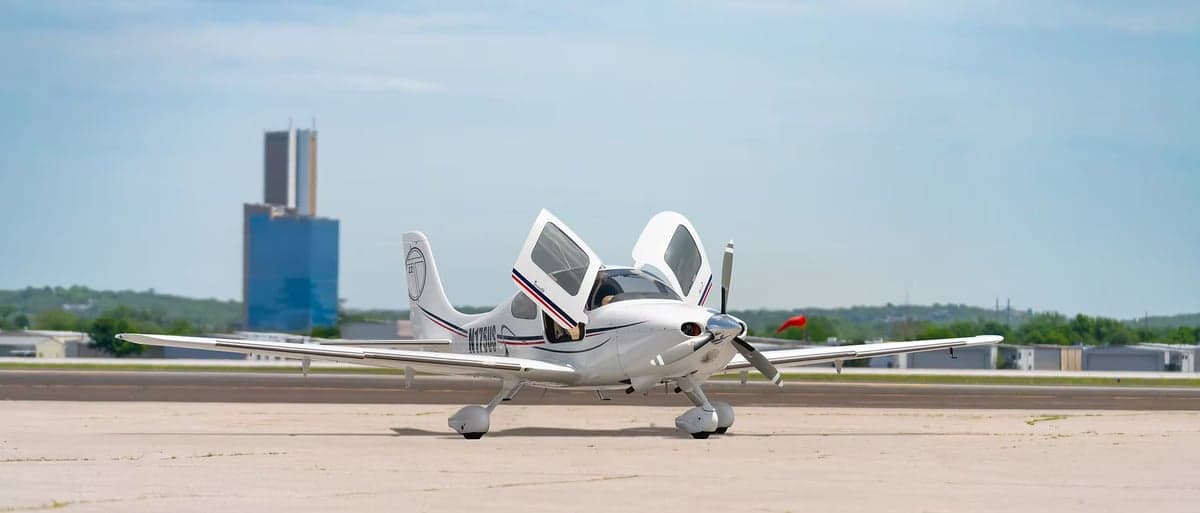 A Cirrus SR22 aircraft is parked on the tarmac with its doors open.