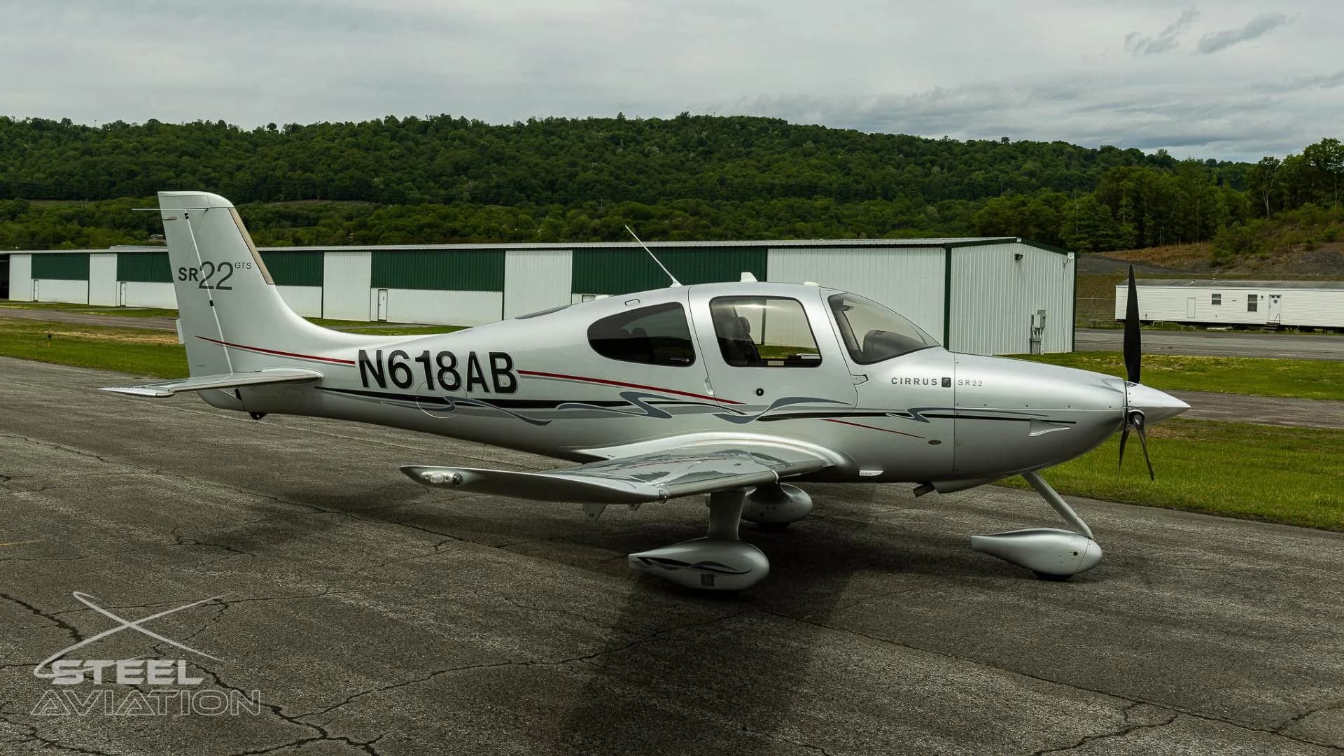 A silver Cirrus SR22 GTS aircraft with registration N618AB parked on an tarmac, viewed from the front-right side.