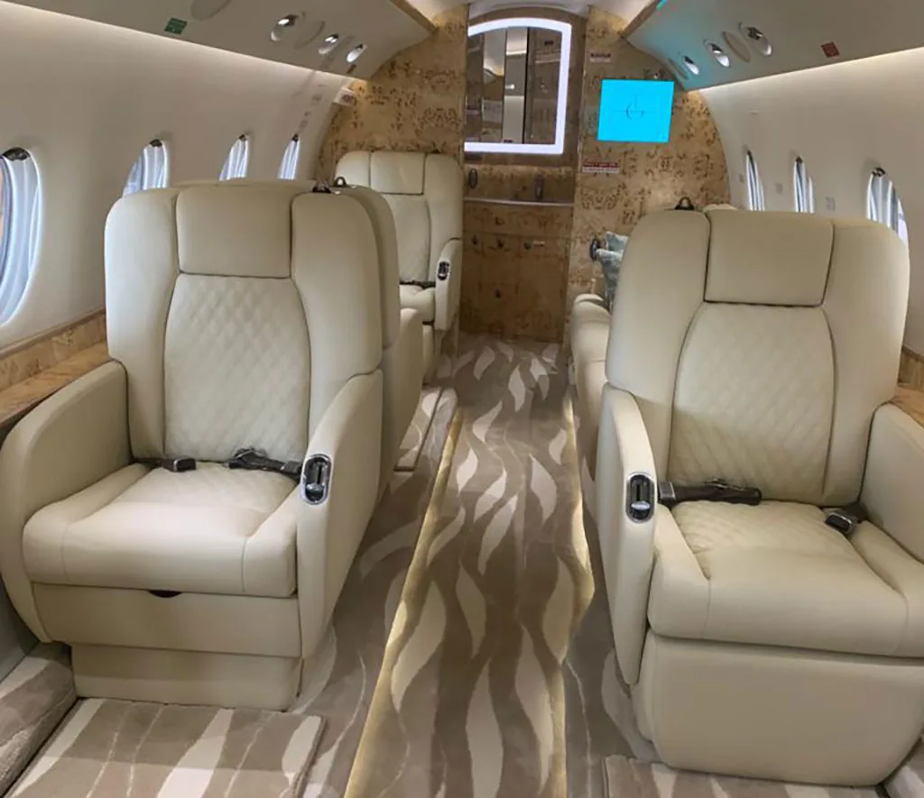A slightly different angle of the private jet cabin interior, highlighting the cream leather seats and the patterned carpet.