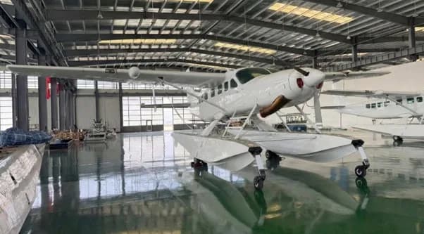 A white floatplane with pontoons is parked inside a large hangar.