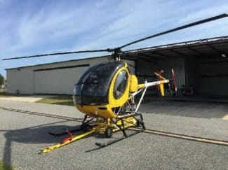 A yellow and black helicopter sits on the tarmac in front of a hangar.