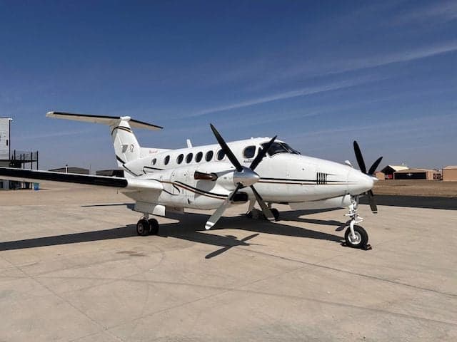 A white King Air 350 is parked on the tarmac on a sunny day.