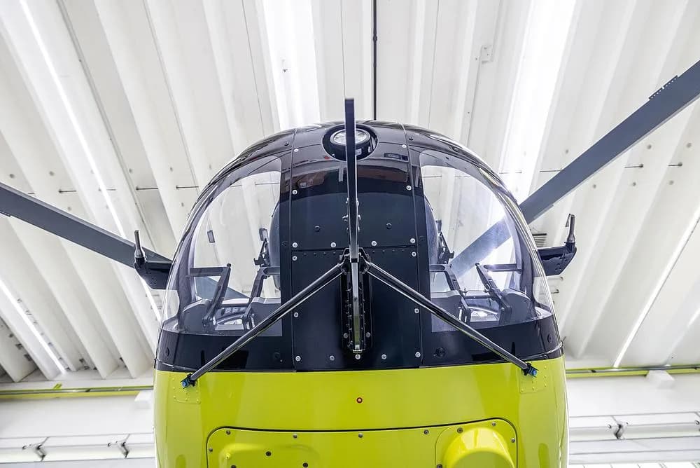A close-up view of the front of a yellow Airbus H135 helicopter, focusing on its transparent cockpit and rotor mast.