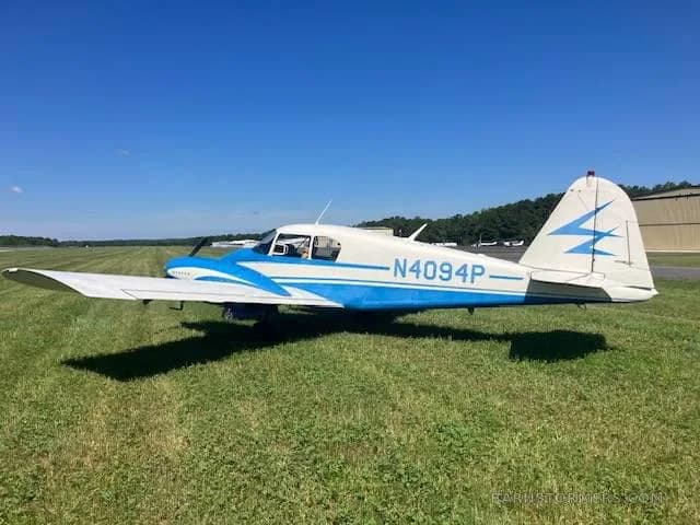 A white and blue Piper Pacer (N4094P) is parked on a grassy field next to a runway.