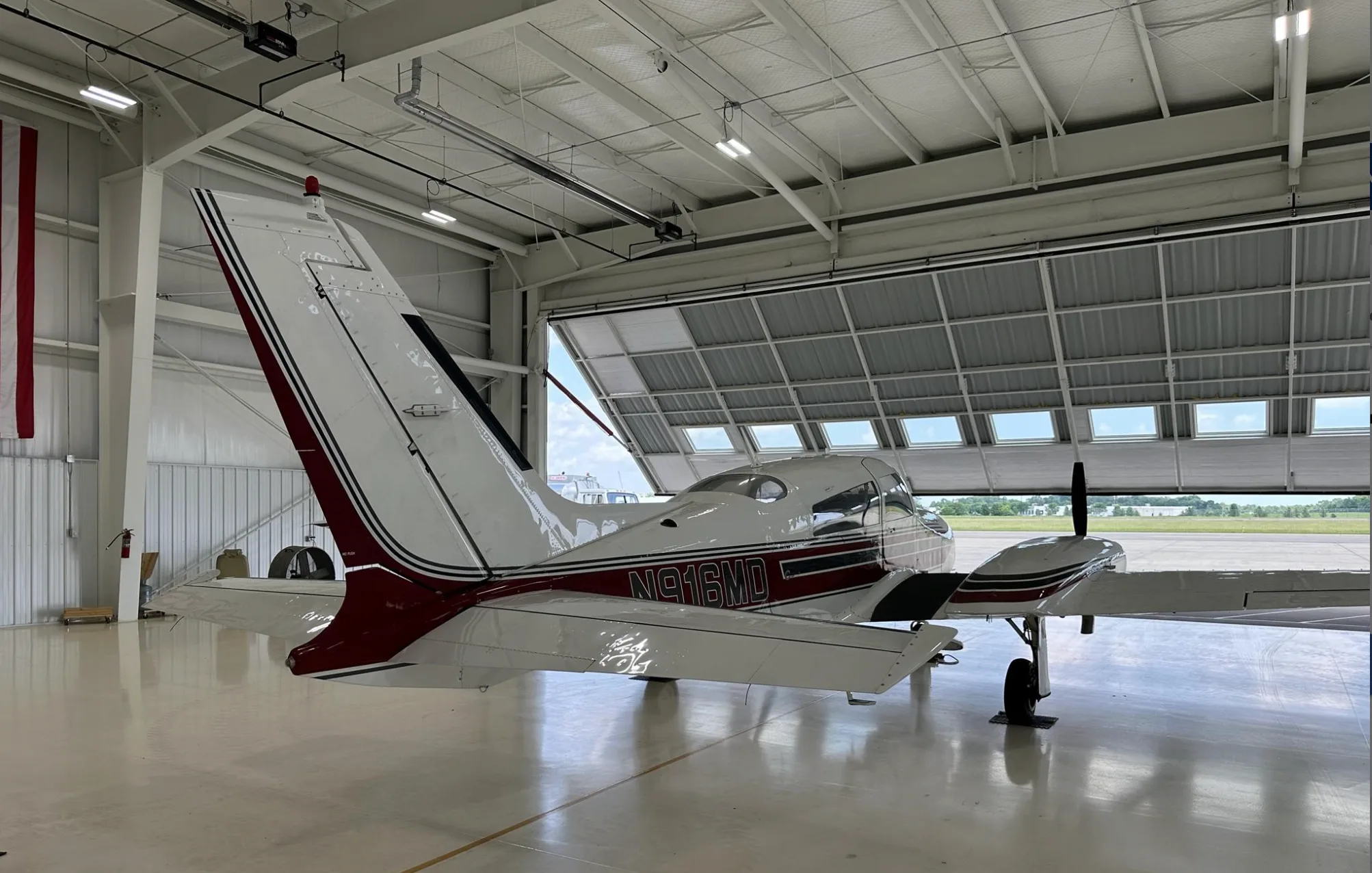 A rear-quarter view of the white and maroon twin-engine aircraft, N916MD, partially exiting a hangar.